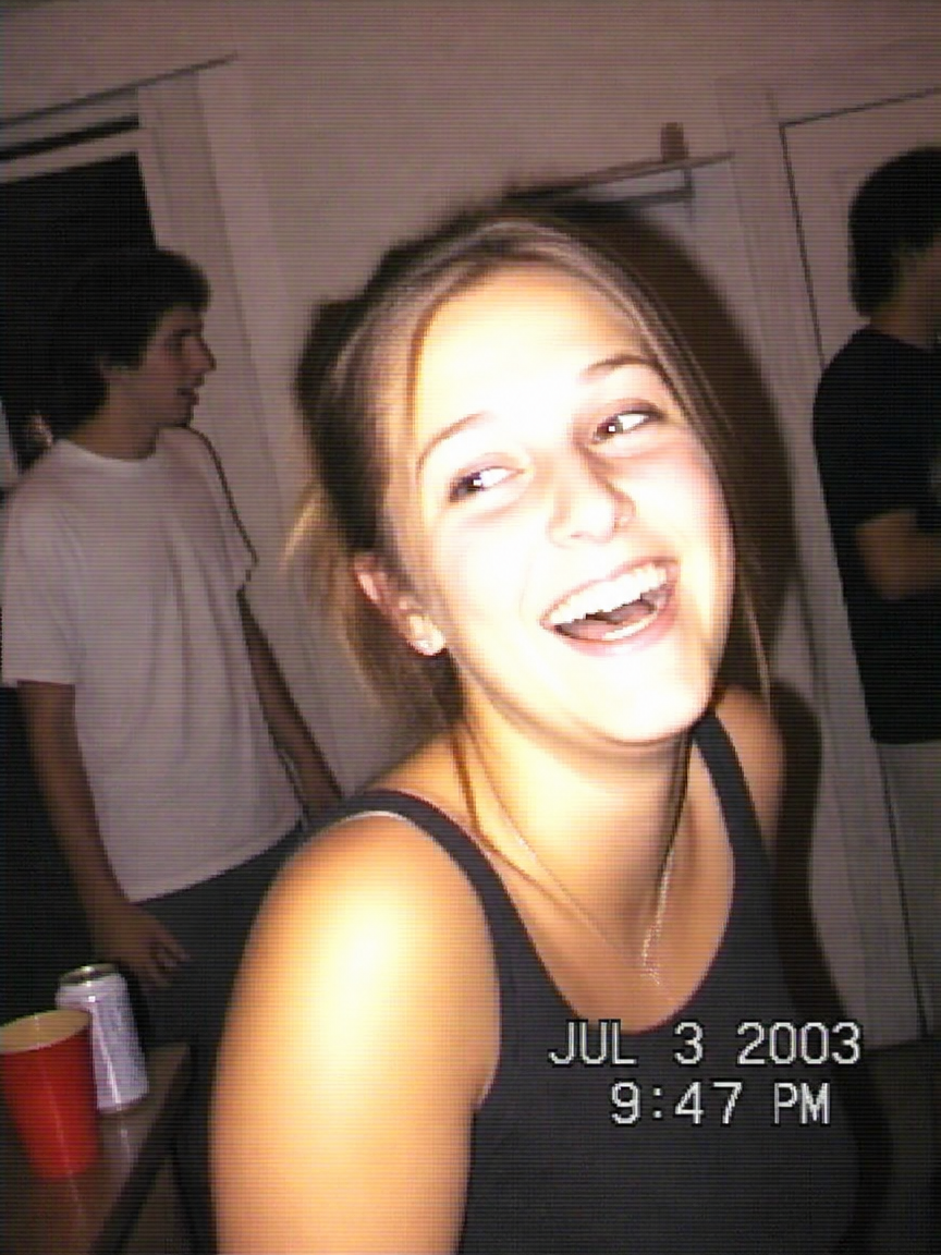 Candid party portrait shot like a cheap 2003 camcorder — harsh flash, video grain, VHS color cast, timestamp burned in.